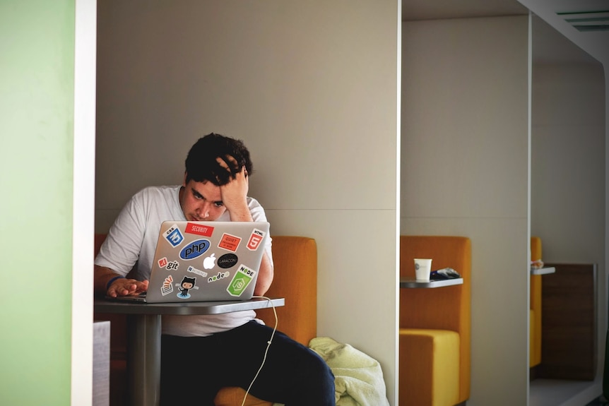 A man looks exasperated as he uses an Apple laptop. 