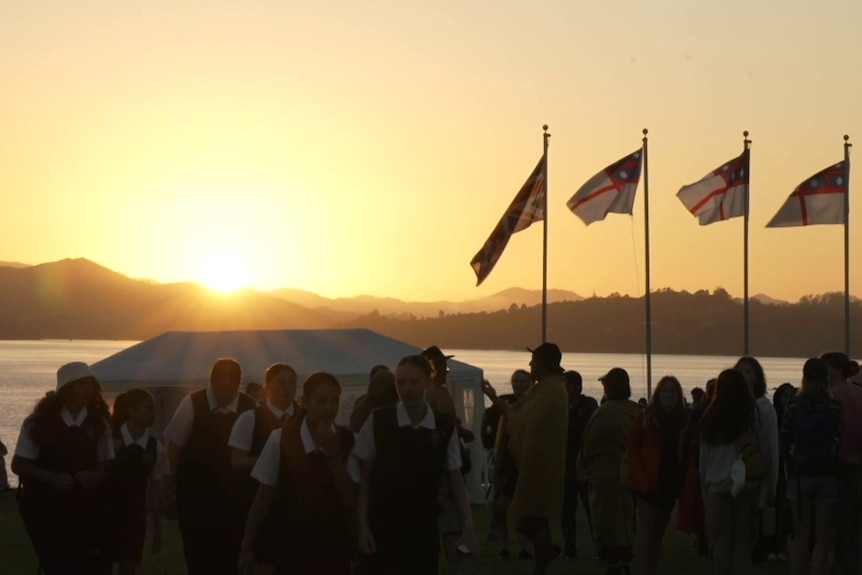 School children silhouetted against the sunrise, with flags waving in the background