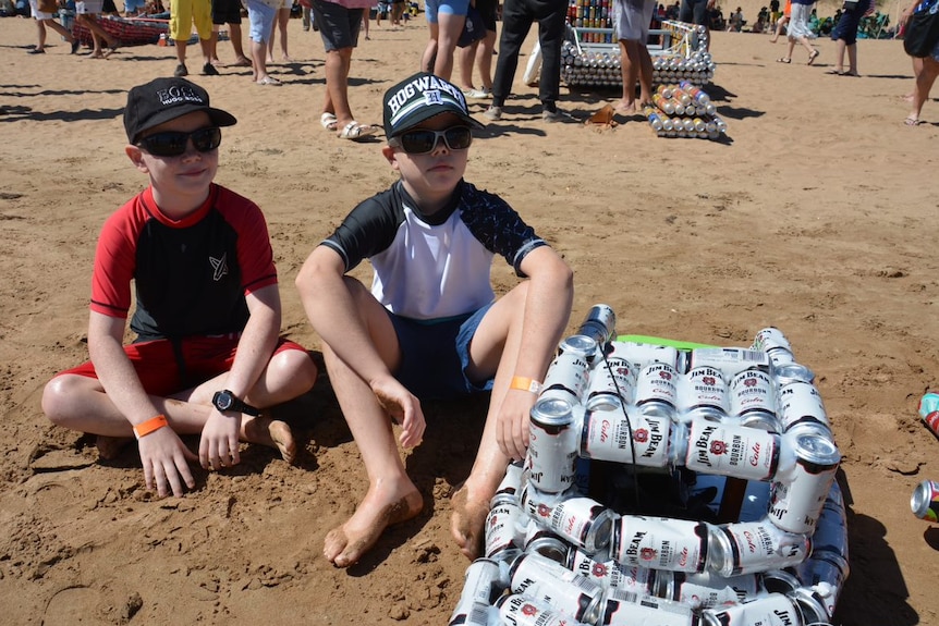 Two young boys with their boat made of cans.