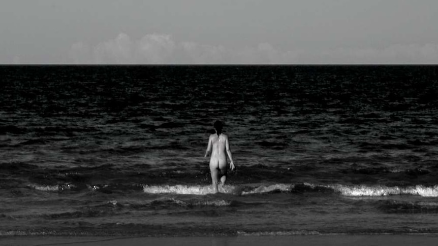 A nude bather wades into the surf