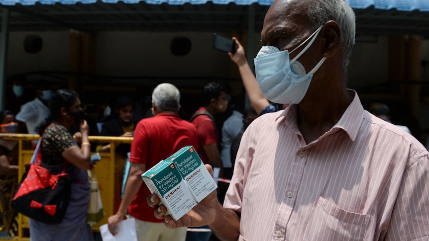 A man wearing a face mask holds a box of the antiviral medication remdesivir