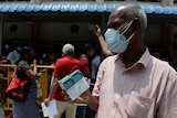 A man wearing a face mask holds a box of the antiviral medication remdesivir