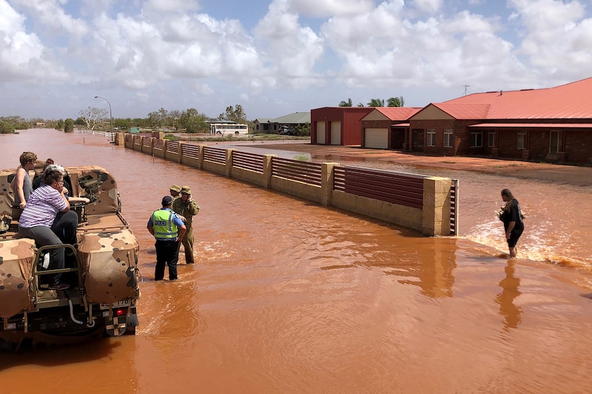 People sit on the back of an Army vehicle in floodwaters, with police and army personnel alongside.