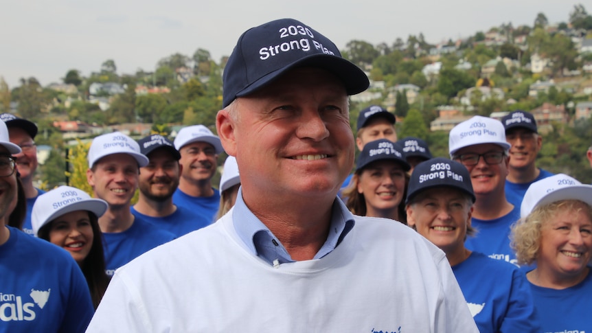 A man wearing a light blue liberal shirt and a cap that reads '2030 strong plan' smiles.