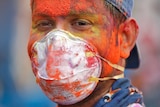 A man covered in colourful dye while wearing a medical face mask