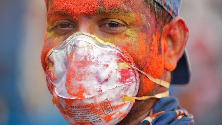 A man covered in colourful dye while wearing a medical face mask