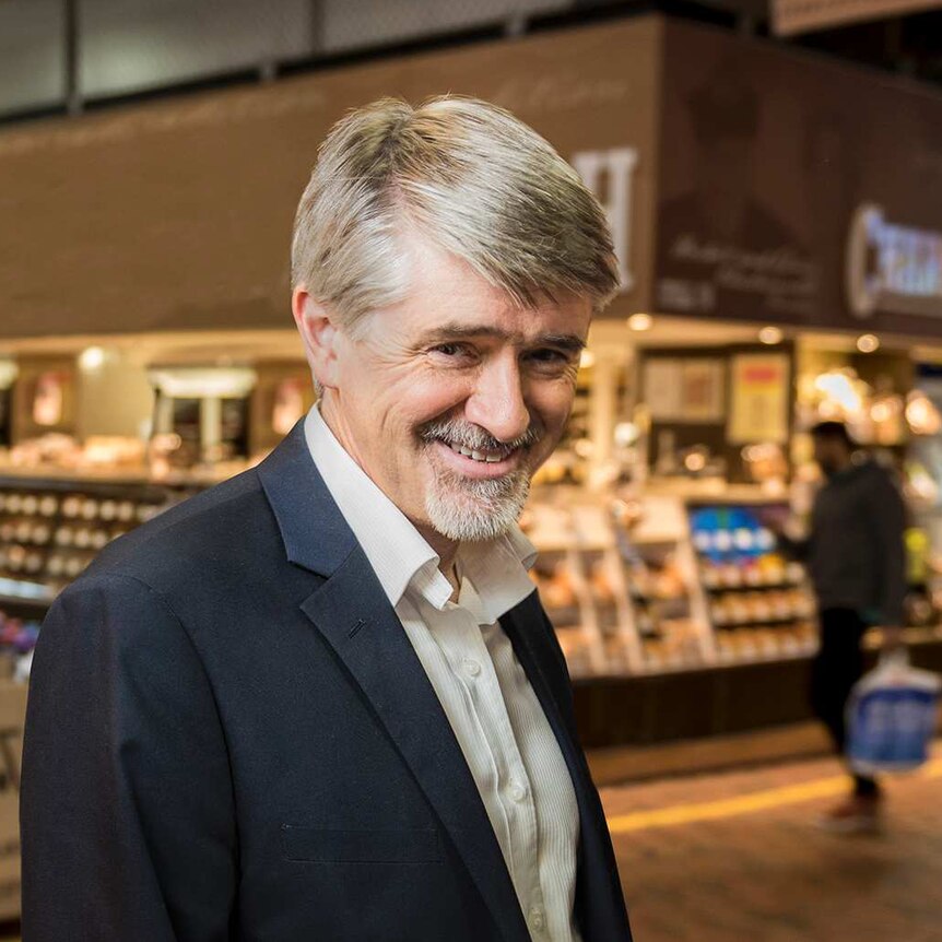A man with short, grey hair and a beard standing in Adelaide Central Market near a bakery.