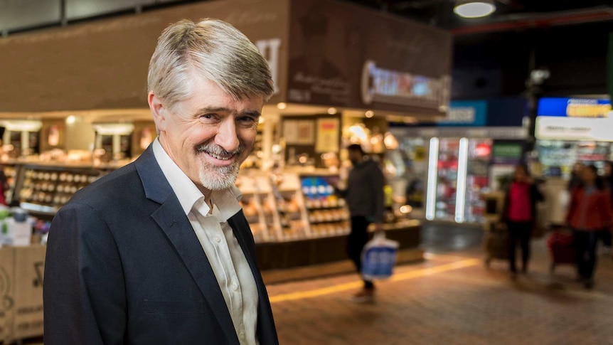 A man with short, grey hair and a beard standing in Adelaide Central Market near a bakery.