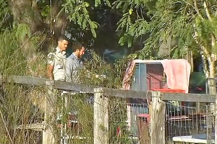 Two police officers walk through the yard of a property in Tarampa, Queensland.