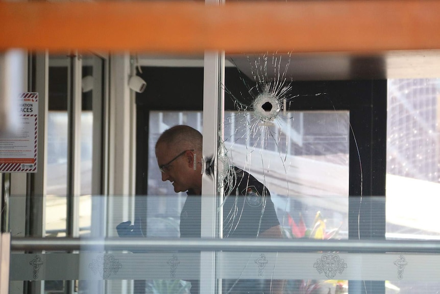 A police officer inside a venue near where a bullet hole is visible in a window