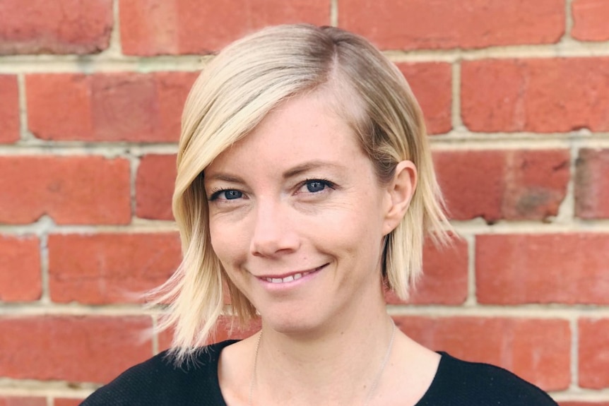 A woman with blonde hair, wearing a black blouse smiles for a portrait