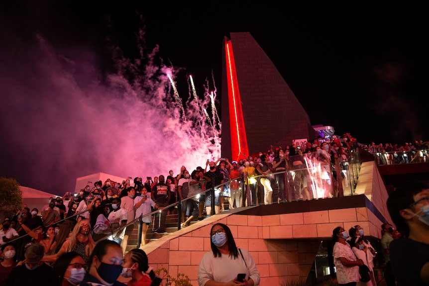 A picture of a crowd standing on stairs with fireworks overhead.
