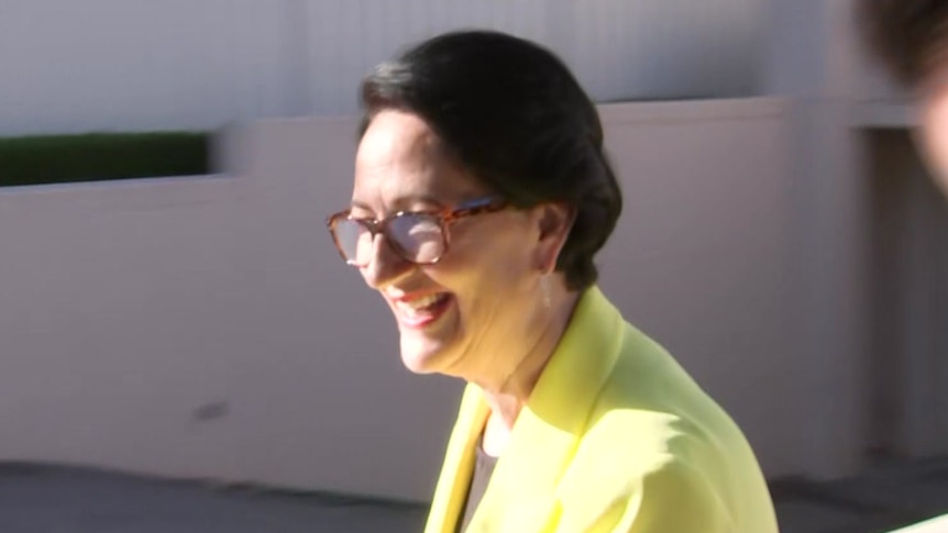 A woman with black hair wearing a yellow jacket walking in a sunken driveway