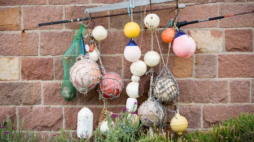 A random collection of sun-bleached buoys hang against a pink granite wall.