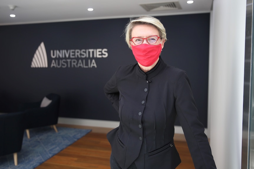 A woman wears a red face mask standing in an office.