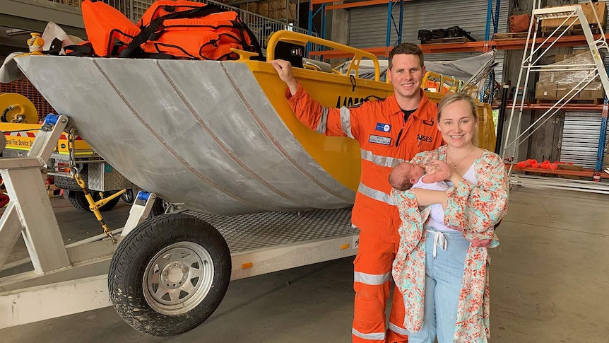 Reece, Kate and baby Harrison stand beside the boat that SES volunteer Reece Booij used to rescue people.