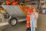 Reece, Kate and baby Harrison stand beside the boat that SES volunteer Reece Booij used to rescue people.