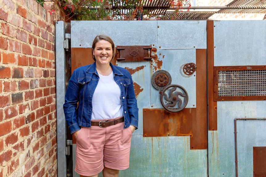 Financial educator and author Lacey Filipich smiles while standing next to a brick wall.