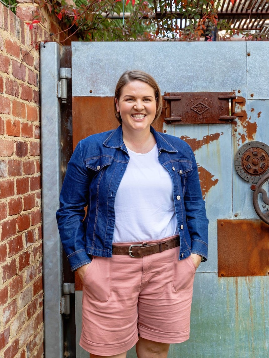 Financial educator and author Lacey Filipich smiles while standing next to a brick wall.