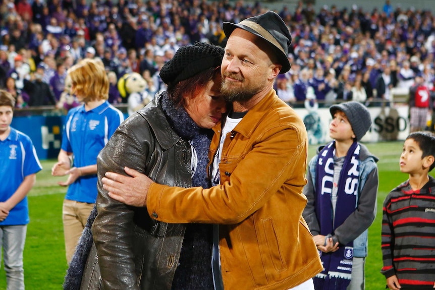 Rin Norris is hugged by Anthony Maslin as they stand on the field of Subiaco Oval in front of a row of children and the crowd.