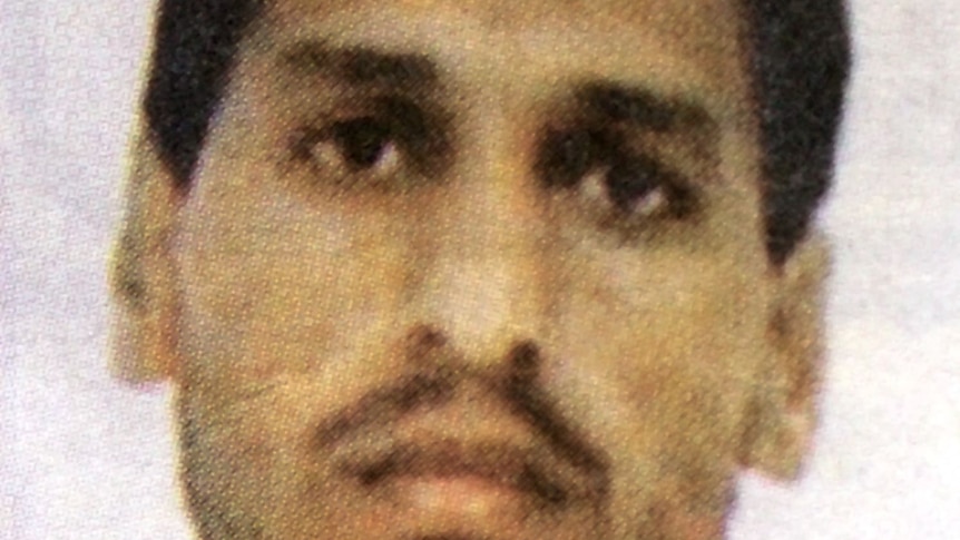 A close up, blurry photo of a man with a moustache and brown eyes.