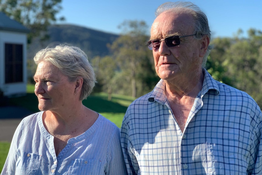 A couple stand in a field with a bright sun above.