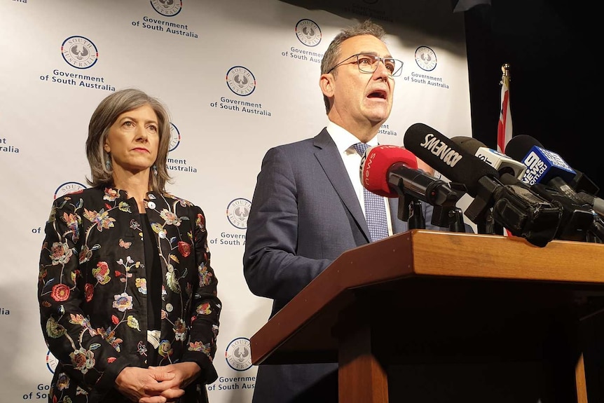 South Australian Premier Steven Marshall speaks to media at a podium as SA Health's Nicola Spurrier looks on.