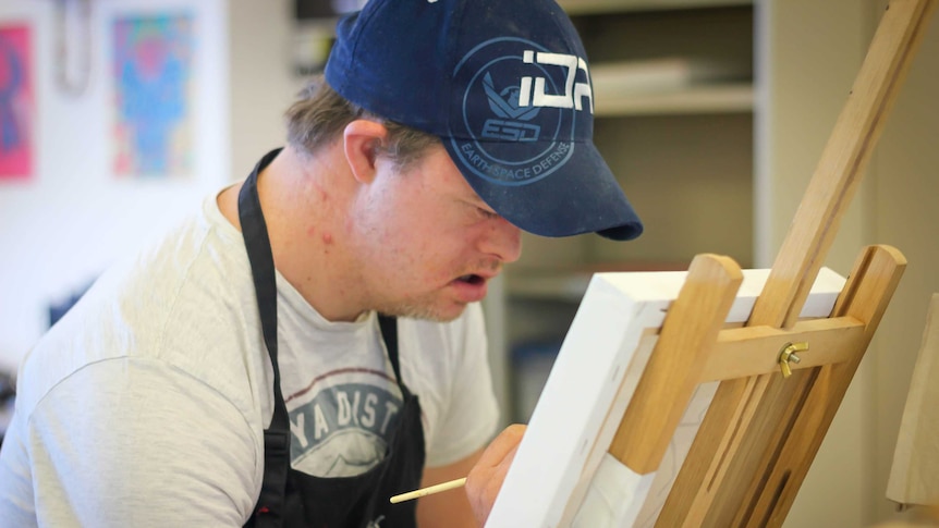A 33-year-old man with Down syndrome paints on an easel during an art class.