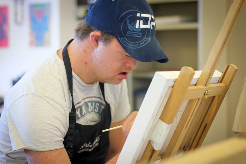 A 33-year-old man with Down syndrome paints on an easel during an art class.