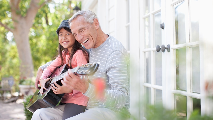 an older man teaches a young girl how to play guitar