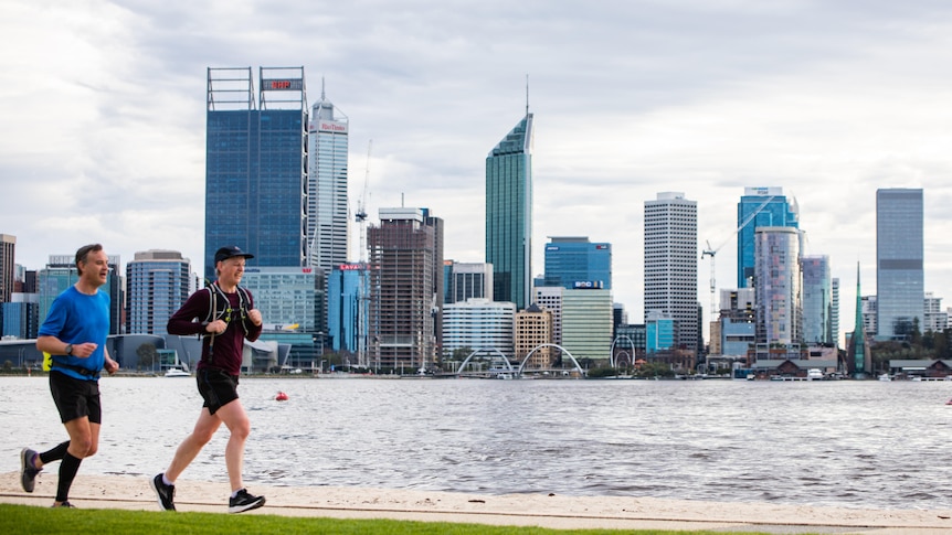 Two men jogging on a footpath next to a river with the Perth city skyline on the other side.