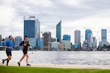 Two men jogging on a footpath next to a river with the Perth city skyline on the other side.