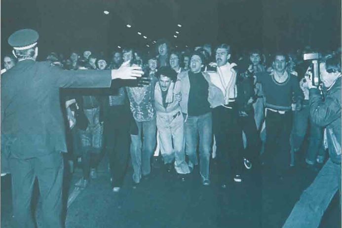 a black and white picture of people protesting on a street standing in front of a policeman