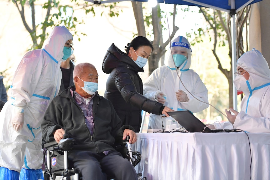 People register for tests at a COVID-19 testing site where staff are wearing white protective suits.