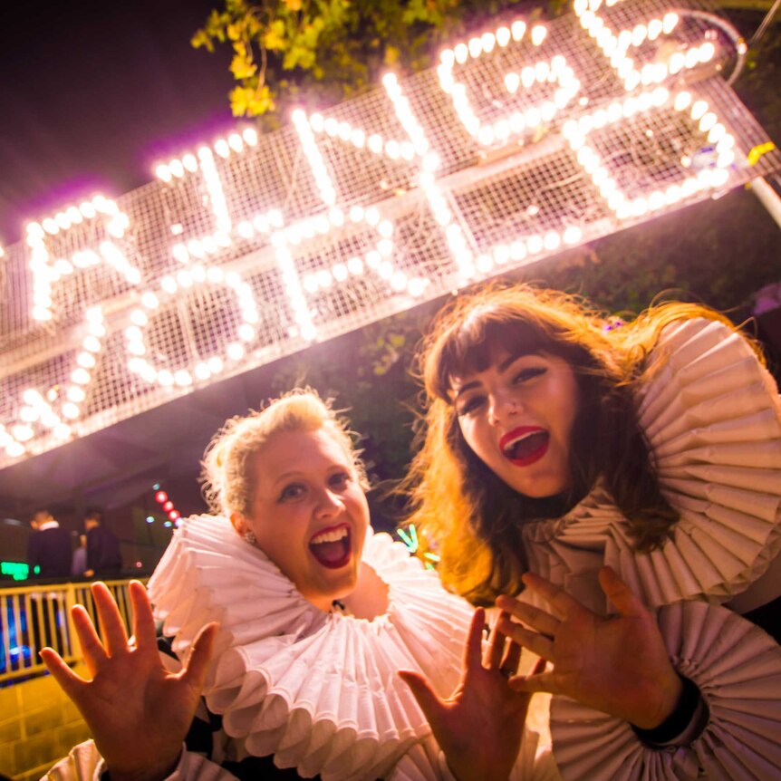 Two women pose for the camera in front of a lit-up Fringe World sign.