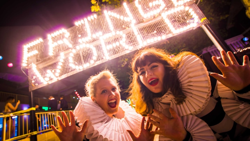 Two women pose for the camera in front of a lit-up Fringe World sign.