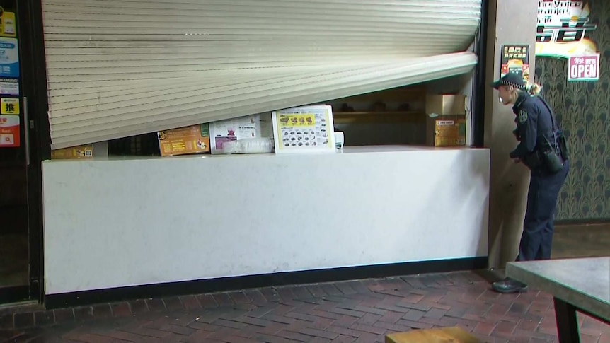 A police officer stands in front of a broken roller window.