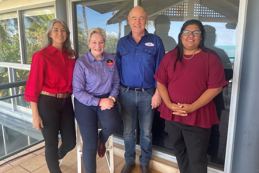 Four people in coloured shirts stand in front of window