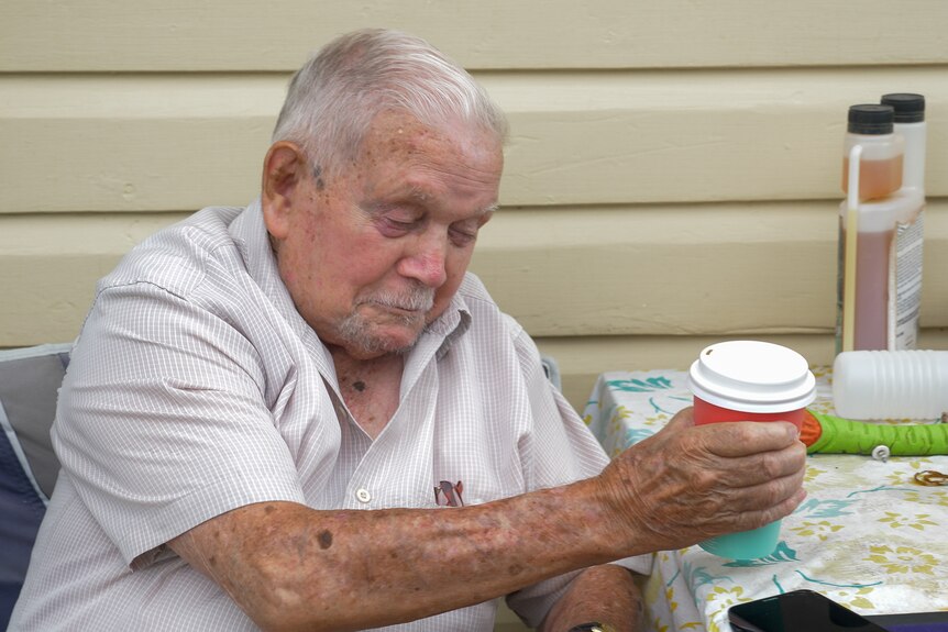 Kevin sits holding a coffee, St George, Queensland 2024.