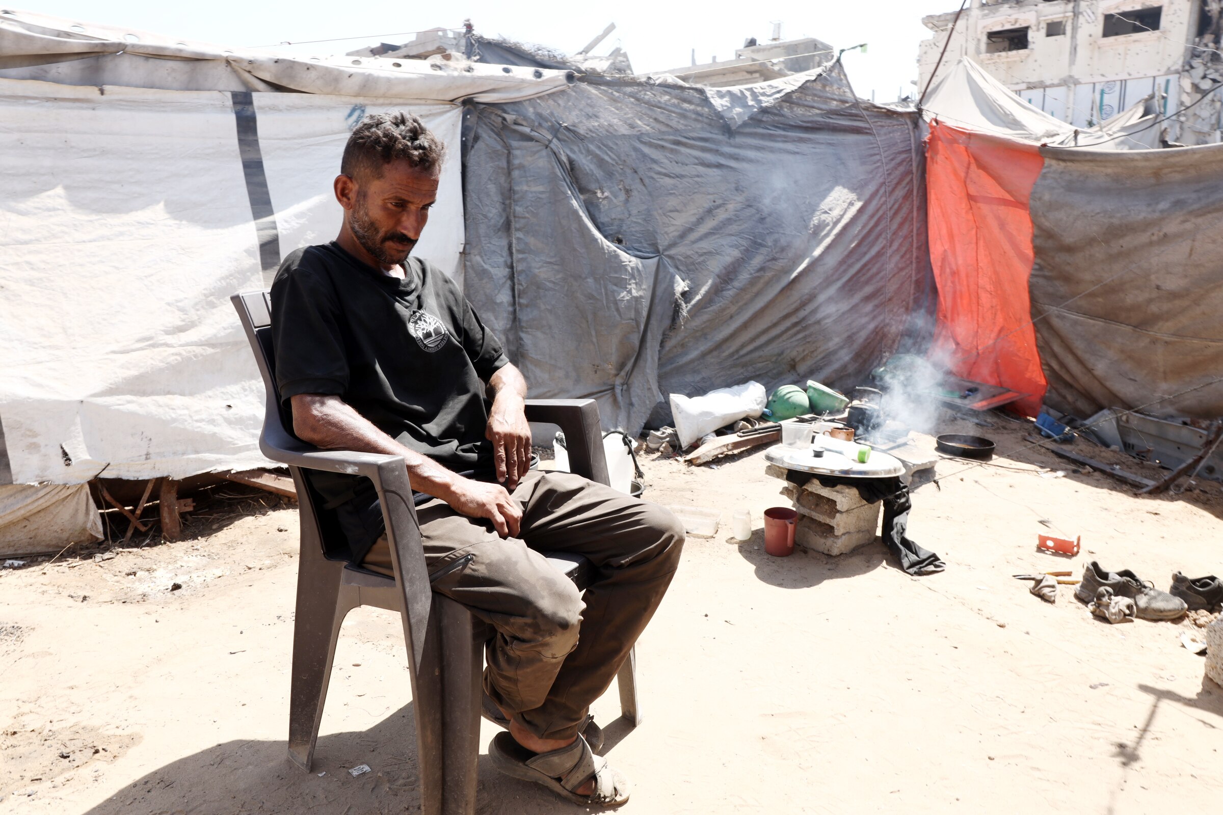 A man sits in a plastic chair among tents. 