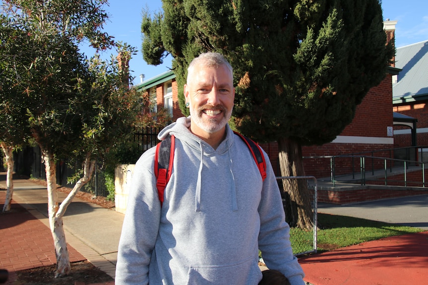 A smiling man in front of a school