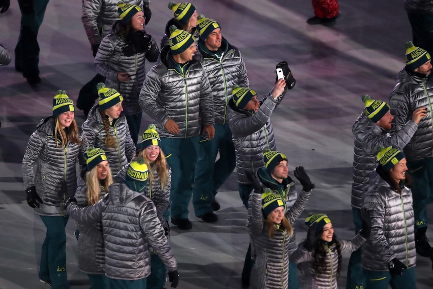 A group of Australian athletes wearing parkas and beanies smile and wave as they walk at the Winter Olympics opening ceremony.