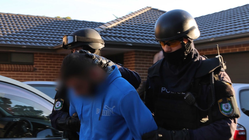 Two police officers hold a man by the arms outside a house.