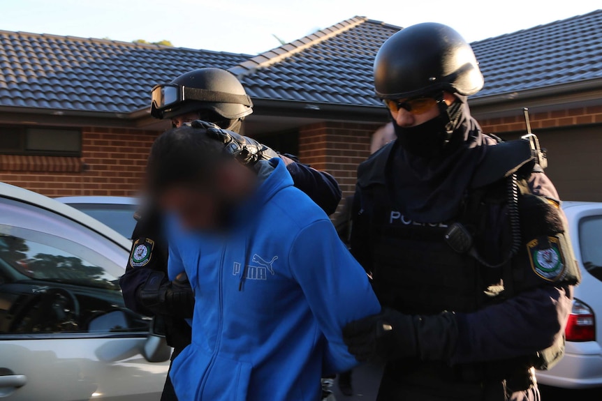 Two police officers hold a man by the arms outside a house.