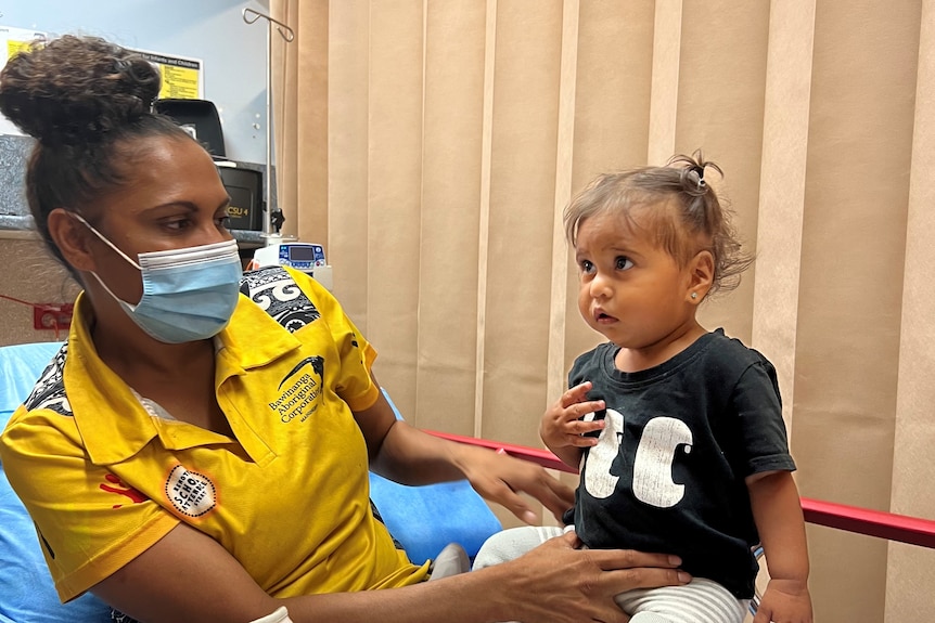 An Indigenous mother and child sit on a hospital bed. 