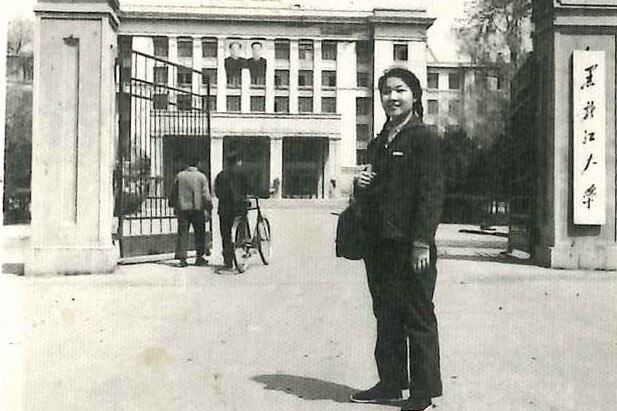 A black and white photo of Shuang Liu standing in front of Heilongjiang University.