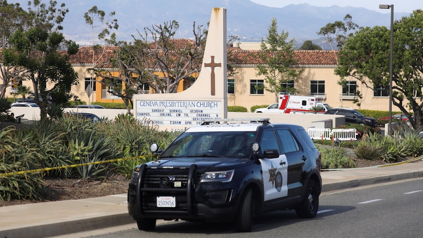 A police car is parked outside a church with an ambulance and police tape in the background.