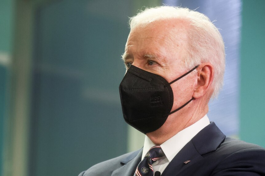 Joe Biden wearing a black mask looks off in the distance.