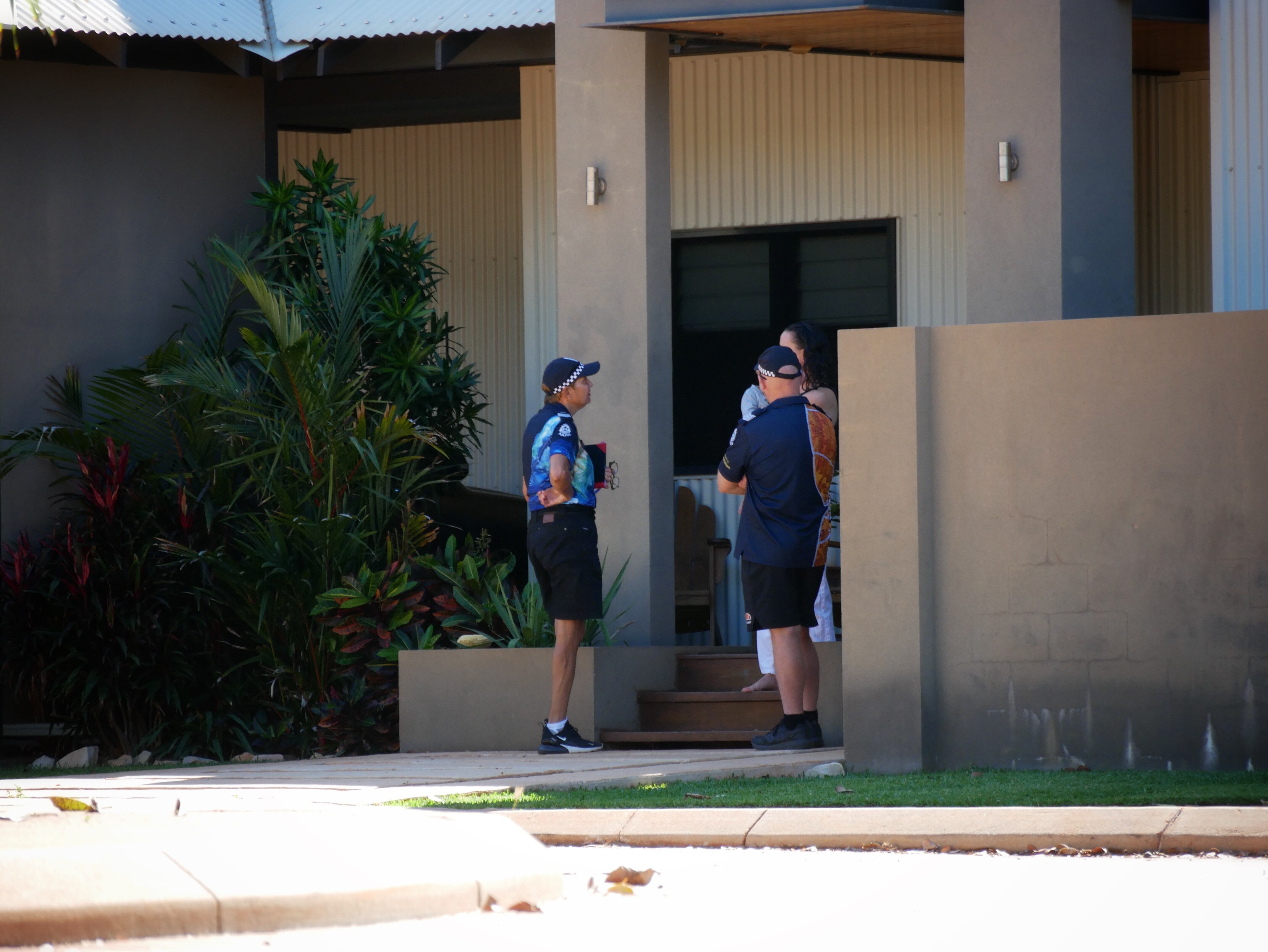Two officers speak to residents outside a house in Broome