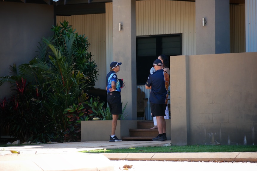 Two officers speak to residents outside a house in Broome